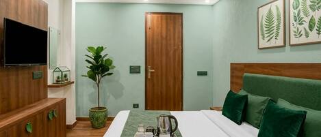 A hotel room with a bed, a television, a plant, and artwork on the wall.