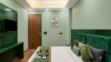 A bedroom with a bed, a TV, a wooden door, and a green wall.