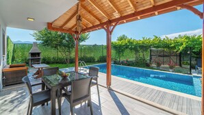 An outdoor patio with a pool, wooden pergola, and outdoor furniture.