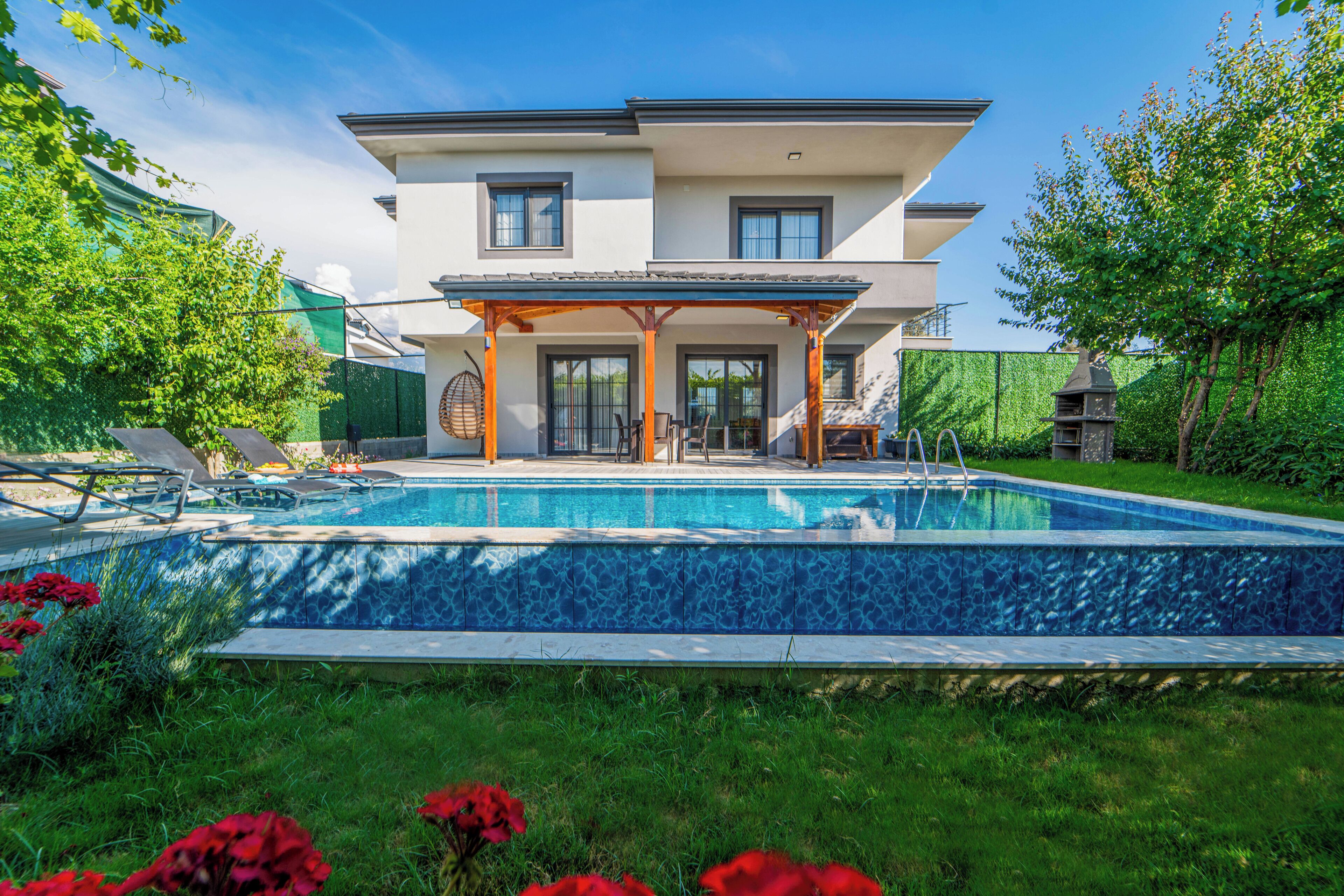 A two-story house with a swimming pool, a covered patio, and a garden.