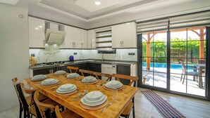 A modern kitchen with white cabinetry, a dining table set for six, and a view of a swimming pool through large sliding glass doors.