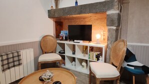 Een woonkamer met een open haard, twee rieten fauteuils, een ronde houten salontafel en een televisietoestel.