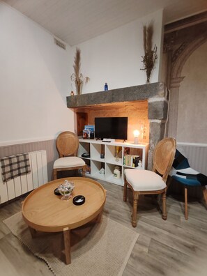 Ein Wohnzimmer mit Kamin, zwei Korbsessel, einem runden Holztisch und einem Fernseher.