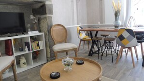 Een woonkamer met een televisie, een boekenkast, een eethoek met stoelen en een ronde houten tafel.