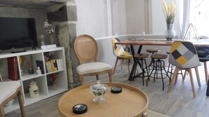 Ein Wohnzimmer mit Fernseher, Bücherregal, Essbereich mit Stühlen und einem runden Holztisch.
