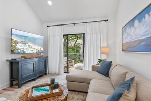 Ein Wohnzimmer mit Fernseher, Sofa und Blick auf einen Strand durch das Fenster.