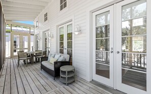 Eine überdachte Veranda mit Holzdeck, einer Couch, einem Tisch und Stühlen.