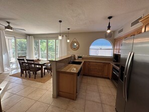 A kitchen with a central island, a refrigerator, wooden cabinets, a dining area with chairs, and a large window. - Beautiful 2 BR. 2 bath, Sun & Sea Retreat, Rainbow Beach Club Sint Maartan .  (Cupecoy)