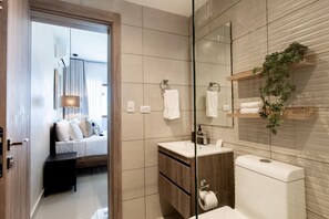 A modern bathroom with a glass shower enclosure, a wooden vanity, a toilet, and a bed visible through an open door. - First floor, 4 pools, beach nearby, and gym (Punta Cana)