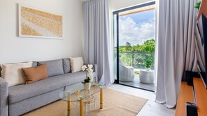 Een moderne woonkamer met een grijze bank, een glazen salontafel en uitzicht op groen via een schuifdeur.