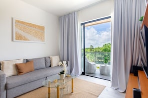 Ein modernes Wohnzimmer mit einem grauen Sofa, einem Glastisch und Blick auf Grün durch eine Schiebetür.