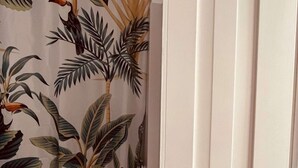 A bathroom with a shower curtain featuring a tropical plant design, a white door, and a wooden towel rack. - Suite Rosa, Portas Residence (Ponta Delgada)