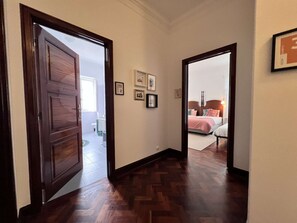 A hallway with wooden flooring leading to a bedroom with a bed and a nightstand. - Suite Rosa, Portas Residence (Ponta Delgada)