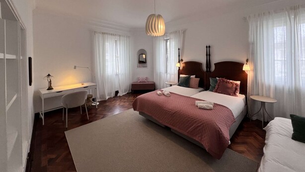A bedroom with a large bed, bedside tables, a desk, and a chair. - Suite Rosa, Portas Residence (Ponta Delgada)