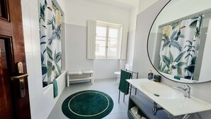 A bathroom with a white sink, a mirror, a toilet, a bench, and a green rug. - Suite Rosa, Portas Residence (Ponta Delgada)