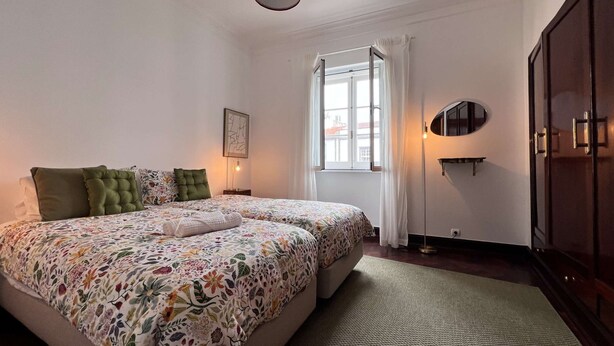 Ein Schlafzimmer mit Bett, Nachttisch, Fenster mit Vorhängen, Stehlampe und Kleiderschrank.