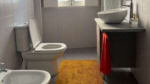 Ein Badezimmer mit Toilette, Bidet und Waschbecken, ein Fenster mit Blick und einem gelben Teppich.