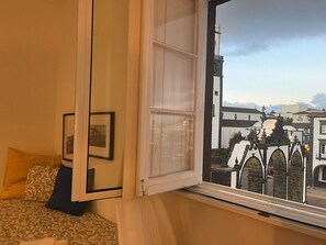 Ein Zimmer mit Bett, einem Fenster mit Blick auf Gebäude und einer Tür.