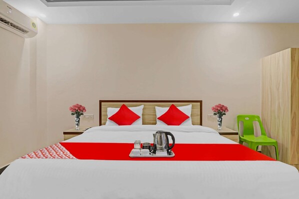 A hotel room with a bed, a nightstand, a green chair, and a tray with a coffee pot and cups.