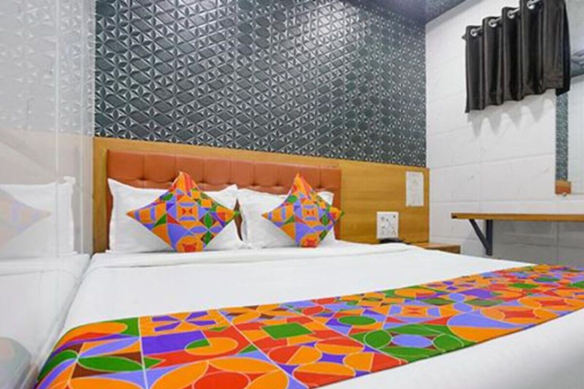 A hotel room with a bed, colorful pillows, a patterned wall, and a window with curtains.
