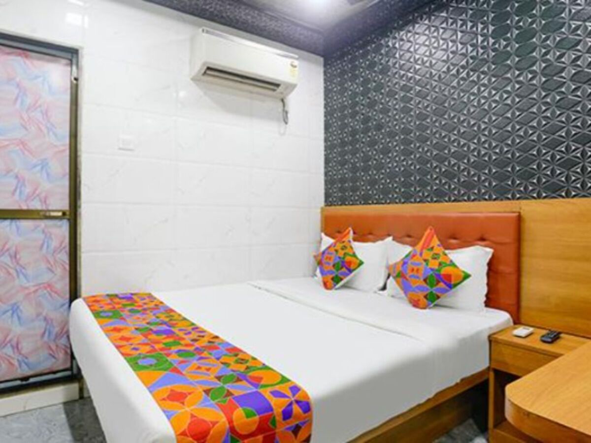 A hotel room with a bed, a nightstand, a wooden headboard, a patterned wall, and an air conditioning unit.