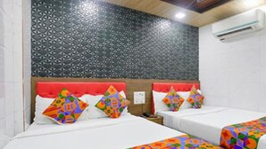 Une chambre d’hôtel avec deux lits, des couvre-lits aux motifs géométriques et aux couleurs vives, une tête de lit rouge et un mur orné de motifs.