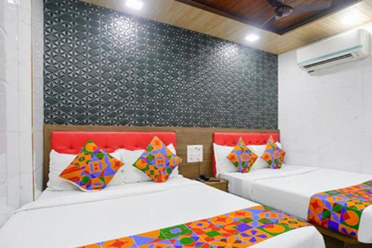 A hotel room with two beds, colorful geometric-patterned bedspreads, a red headboard, and a patterned wall.
