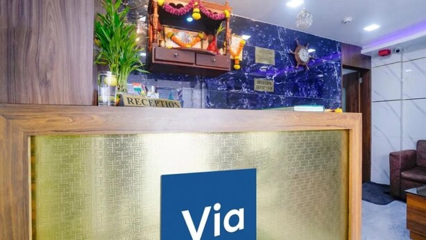 Un comptoir d’accueil orné du logo « Via », un espace d’accueil avec un mur en marbre bleu, une horloge et une plante.