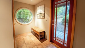 A hallway with a wooden bench, a round window with a bamboo view, and a wooden door with glass panels. - Beautiful Farmhouse & thermal Spa in Forest (Sechelt)