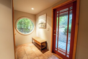 A hallway with a wooden bench, a round window with a bamboo view, and a wooden door with glass panels. - Beautiful Farmhouse & thermal Spa in Forest (Sechelt)