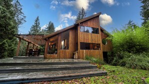 A wooden cabin with a deck, large windows, and a circular skylight. - Beautiful Farmhouse & thermal Spa in Forest (Sechelt)