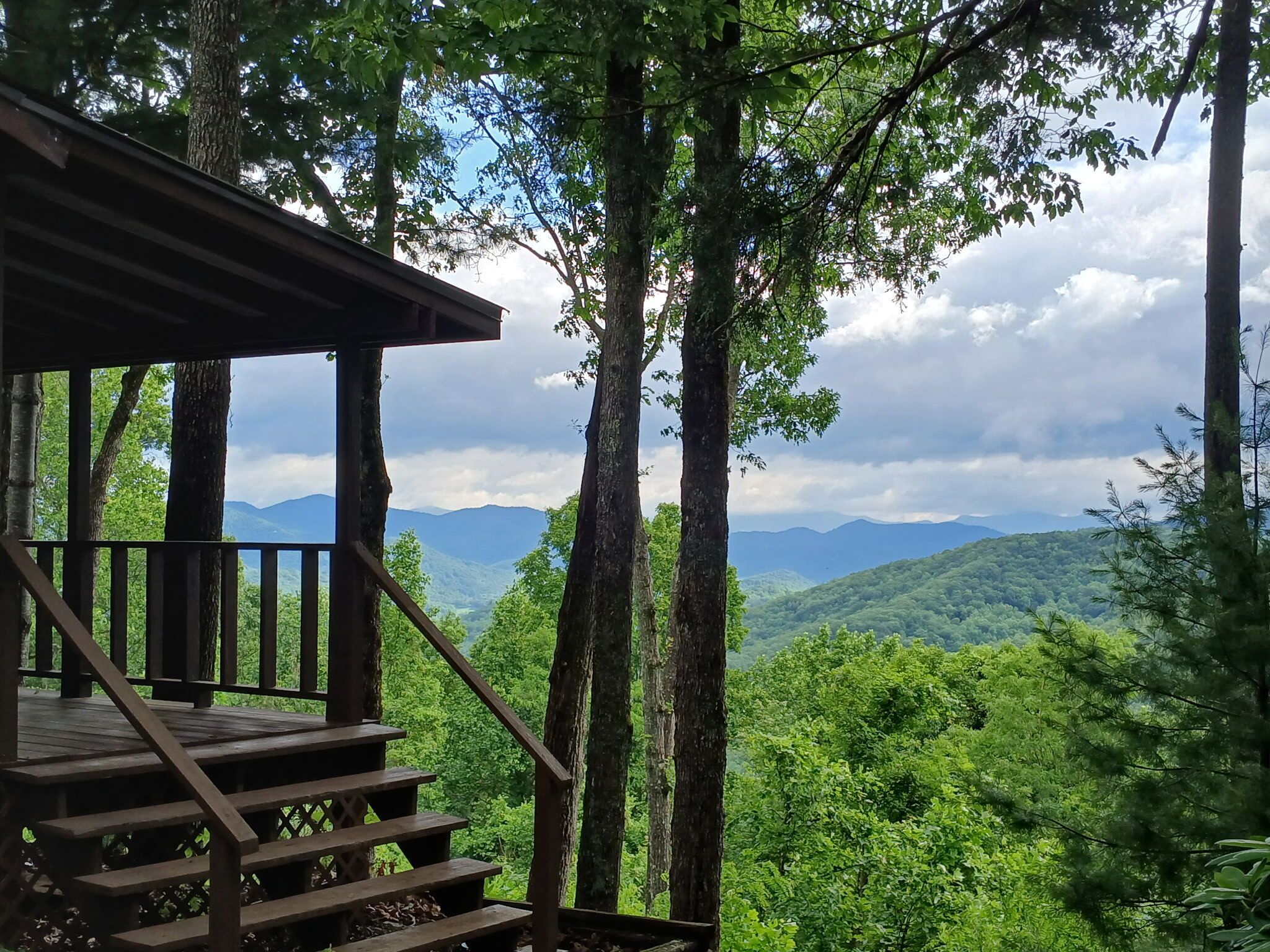A wooden staircase leading to a covered area with a view of a forested mountain range.