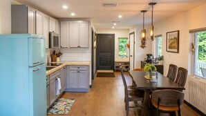 A modern kitchen with white cabinets, a blue refrigerator, and a dining area with a wooden table and chairs. - Serene Andes Retreat: A/C, BBQ & Nature (Andes)