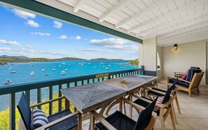 A balcony with a view of boats on a turquoise sea, wooden furniture, and a 'DO NOT LEAN ON RAILINGS' sign.