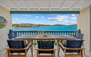 Una mesa y sillas de madera en un balcón con vistas al mar y a barcos.