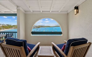 A balcony with two wooden chairs, a small table, and a view of the sea with boats.