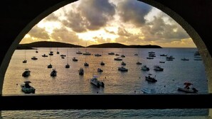 A marina with boats anchored in calm waters, viewed through an arched structure. - Oceanfront steps to beach & yacht club-generator (St. Thomas)