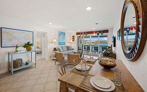 A dining area with a wooden table set for four, a sofa, and a view of the sea through a glass door.