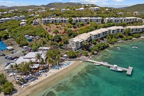 Un resort costero con edificios de varios pisos, una playa y un muelle con barcos.