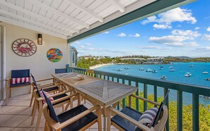 A wooden deck with a table and chairs, overlooking a beach with boats and a clear sky.