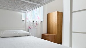 Ein Schlafzimmer mit einem Bett, einem Holzschrank, einem Fenster mit blumigem Vorhang und einer weißen Decke.