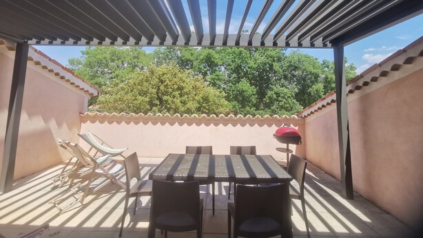 A covered patio with a table and chairs, a grill, and a view of trees. - Spacious apartment near Lake Sainte-Croix, surrounded by truffle oaks. (Sainte-Croix-du-Verdon)