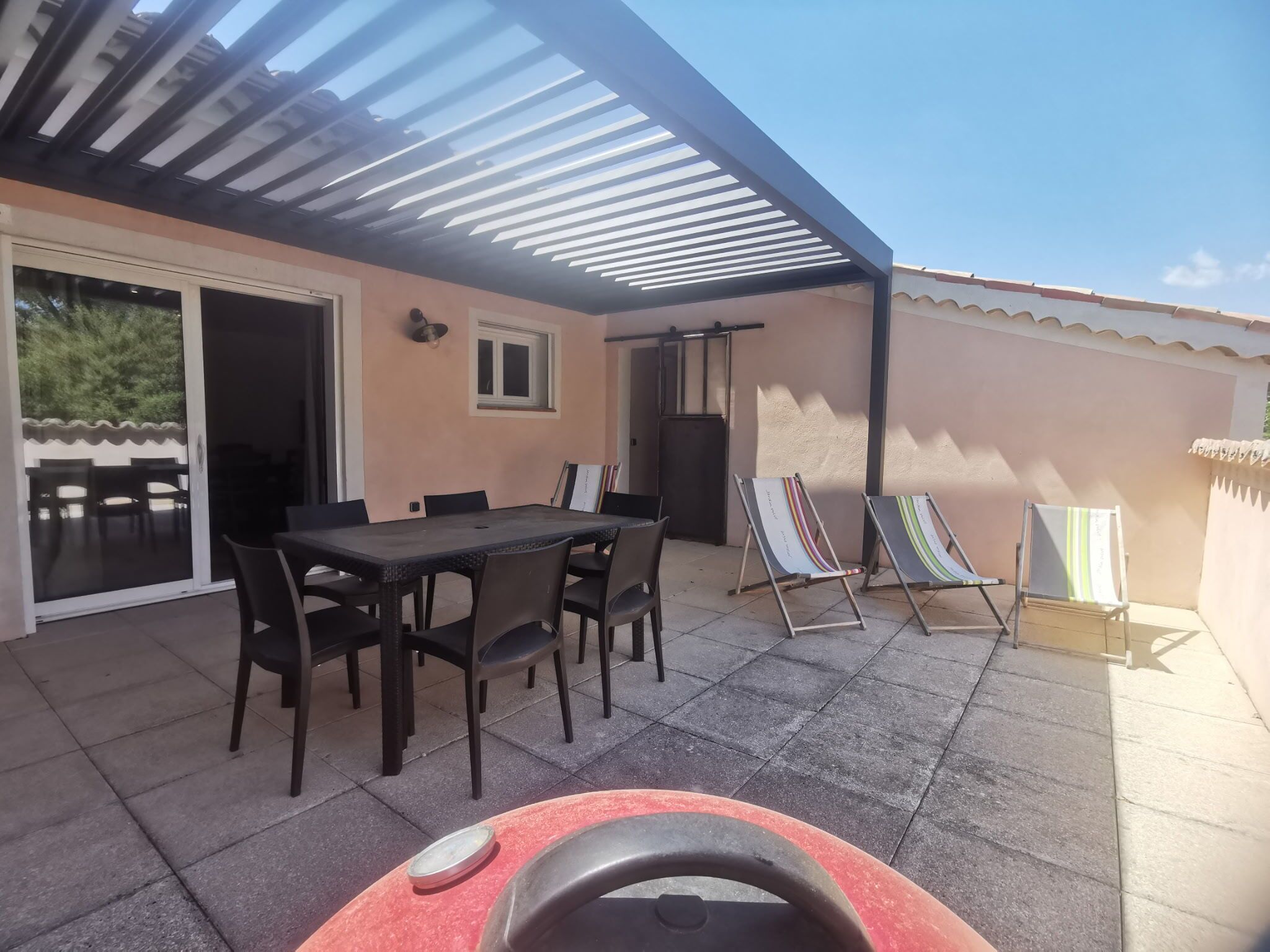 A covered patio with a table and chairs, a grill, and two lounge chairs.
