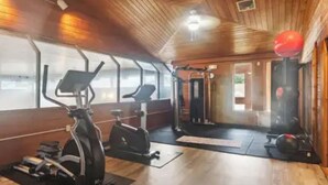 Un gimnasio con equipo de ejercicio, paredes de madera y un ventilador de techo.