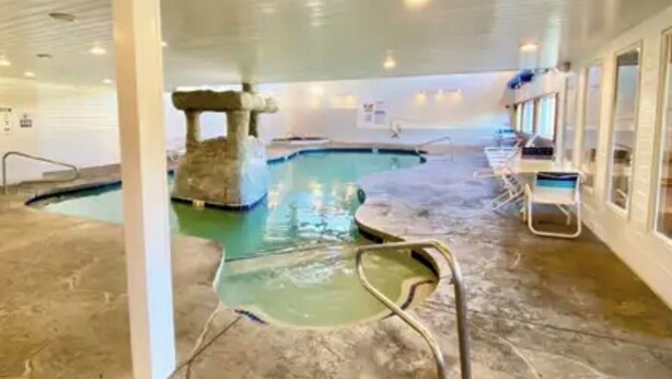 Una piscina interior con una estructura de piedra, asientos junto a la piscina y suelo de baldosas.