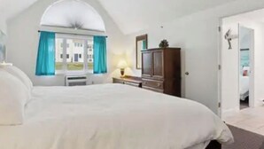 Un dormitorio con una cama grande, una ventana con cortinas, un aparador y una puerta que da a otra habitación.
