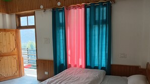 A bedroom with a bed, wooden walls, a window with curtains, and a balcony view.