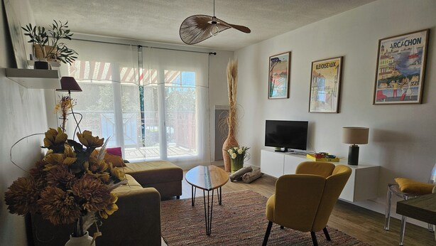 Uma sala de estar com sofá, cadeiras, televisão e uma janela ampla.