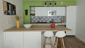 Uma cozinha com ilha de madeira, banquetas brancas de bar, chaleira vermelha e parede verde decorativa.