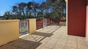Um terraço no telhado com grade de metal vermelha, uma parede amarela e vista para árvores.